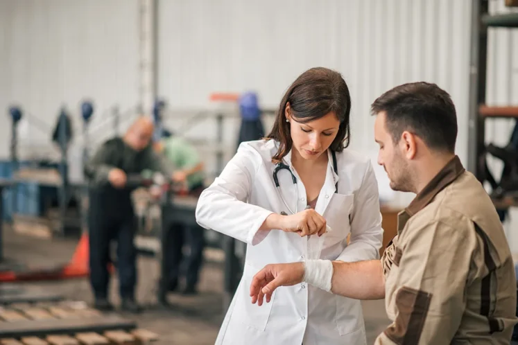 Doctor wrapping an injured worker’s wrist in a factory setting, representing workers' compensation rights.