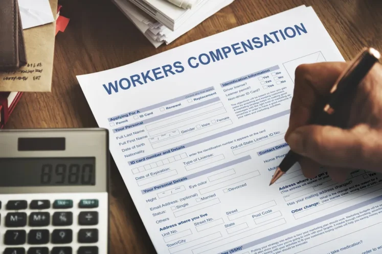 Close-up of a person filling out a workers' compensation form with a calculator on the desk, representing the duration of workers' comp benefits.